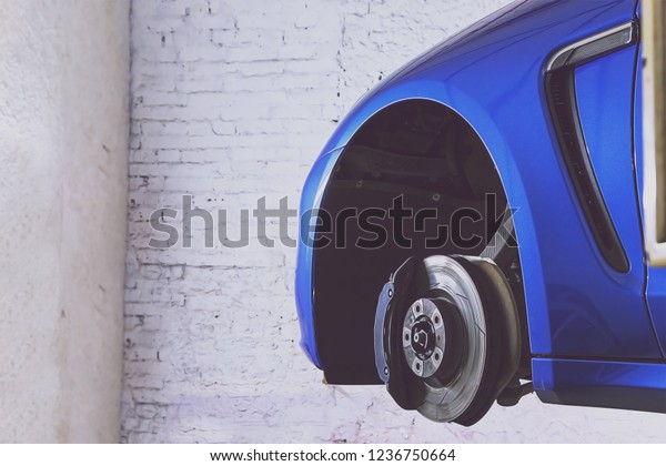 Blue car in the service station for tire,\
suspension and brakes. Standing on a lift against a brick\
wall.\
Wheel replacement service.\
