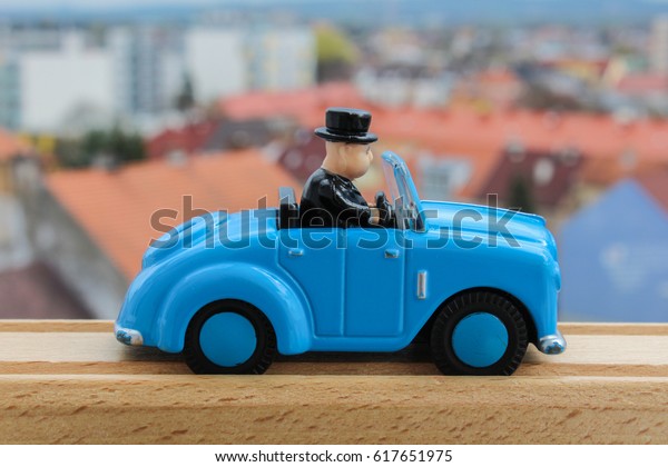 Blue car toy from side in wood rail with\
blured city in background