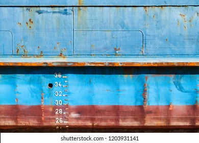 Blue cargo ship hull with red waterline and draft marks, front view, background texture