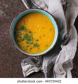 Blue Ceramic Bowl Of Carrot Soup, Served With Onion Chives And Kitchen Towel Over Old Rusty Iron Background. Dark Rustic Style, Overhead View. Square Image