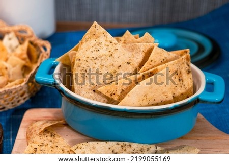 Blue ceramic bowl with handles containing corn chips. Totopos made with fried corn tortillas. Fries served on a plate. Mexican food. Triangle. Close up. Spicy. Salty snack. Nachos. Crunchy appetizer.