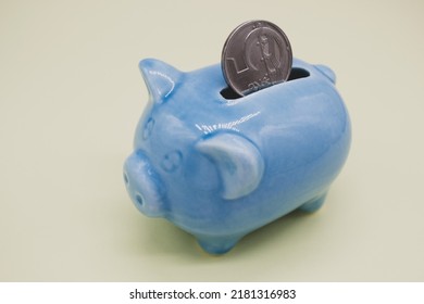  Blue ceramic piggy bank with a suspicious look and a coin of 5 CZK in the hole on a yellow background. Copy space.
