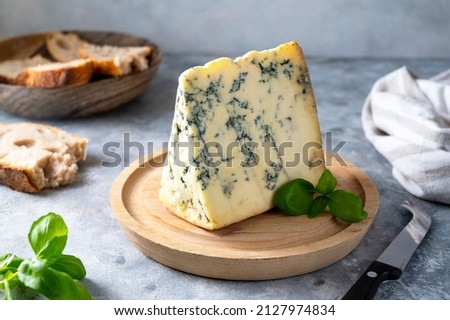Blue cheese, dor blue or roquefort mold cheese slice on cutting board with basil leaves, lifestyle food