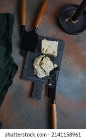 Blue cheese on slate board, cheese knives on rust old heavily worn black navy blue concrete texture or background. With place for text and image