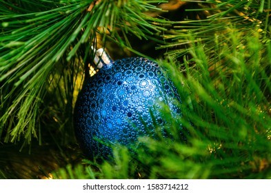 Blue Christmas Ball In The Branches Of A Decorated Christmas Tree. Close-up, Bokeh, Back Drop.