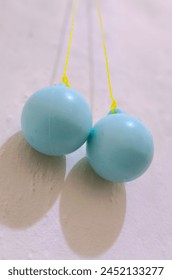 Blue clackers with a vibrant yellow string, suspended on the wall, evoke nostalgic memories of playful days and rhythmic clicks, ready to bring joy to any space.


