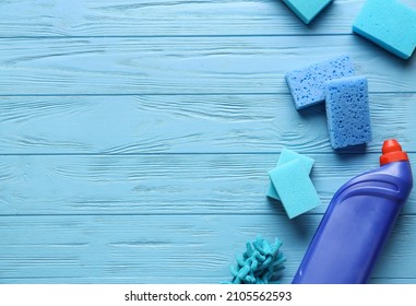 Blue cleaning sponges and bottle of detergent on color wooden background