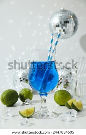 Blue cocktail in glass, limes, ice cubes and disco balls on white background