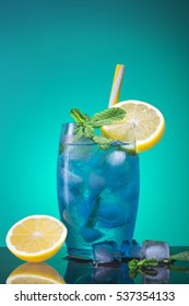 Blue cocktail with a slice of lemon, ice and mint. A glass with a blue lagoon alcohol cocktail on a blue background.