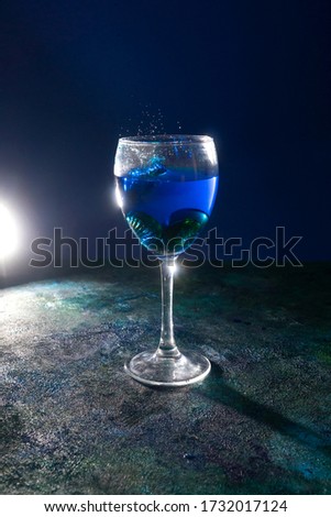 Blue cocktail in wineglass with splash on the black background.