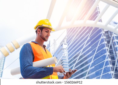 Blue Collar Worker, Engineer Man Work On Digital Tablet, Hold Blue Print, Wear Safety Hat, Stand Near Worksite. Worker Guy Survey A Land For Big Project Of Building Or Estate. Look Determined