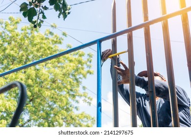 Blue Collar Worker Outdoors Measuring Steel Rods While Installing A Metal Fence.