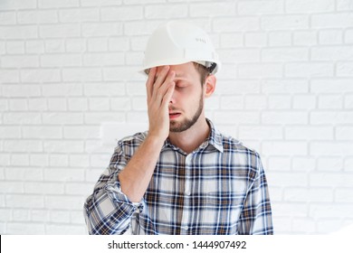 A Blue Collar Worker Wearing A Hardhat Is Covering His Face With His Hand