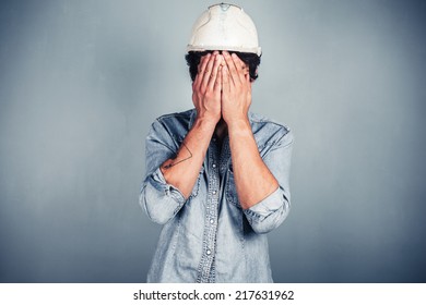 A Blue Collar Worker Wearing A Hardhat Is Covering His Face With His Hands