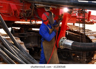 A Blue Collar Worker Welding Earth Moving Equipment On A Construction Site