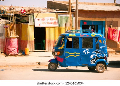 Blue Color Auto Rickshaw (Tuk Tuk) Standing On Dusty Street Of Small Town Of Tigray Region In Front Of Shops Made Of Shipping Containers, Northern Ethiopia, Africa