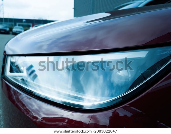 Blue color cast of new xenon\
led laser light of a red luxury car in large car parking\
dealership