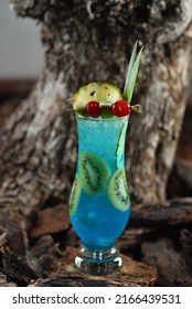 Blue color cocktail with Blue Curacao liqueur and vodka, in a glass glass with ice and fruits, Blue Lagoon on a background of tree bark