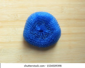 Blue color plastic dish scrubber kept on wooden table - Powered by Shutterstock