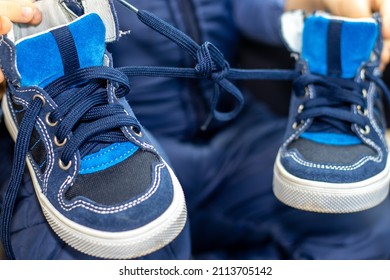 Blue Color Shoes For Kids With Tied Laces, In A Modern Car. Shoes On The Steering Wheel, On The Car's Seat Or In A Boy's Hands. April Fools Day Prank.