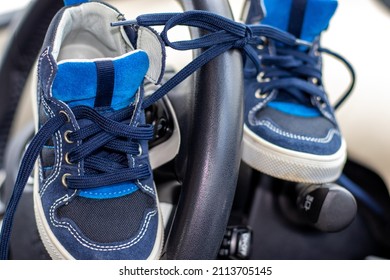 Blue Color Shoes For Kids With Tied Laces, In A Modern Car. Shoes On The Steering Wheel, On The Car's Seat Or In A Boy's Hands. April Fools Day Prank.