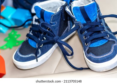 Blue Color Shoes For Kids With Tied Laces, In A Modern Car. Shoes On The Steering Wheel, On The Car's Seat Or In A Boy's Hands. April Fools Day Prank.