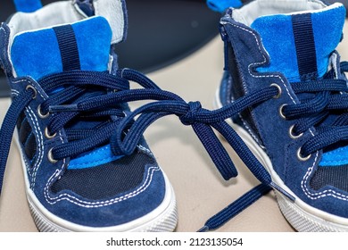 Blue Color Shoes For Kids With Tied Laces, In A Modern Car. Shoes On The Steering Wheel, On The Car's Seat Or In A Boy's Hands. April Fools Day Prank.