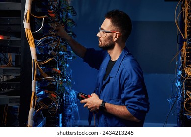 Blue colored lighting. Young man is working with internet equipment and wires in server room. - Powered by Shutterstock