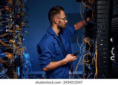 Blue colored lighting. Young man is working with internet equipment and wires in server room. - Powered by Shutterstock