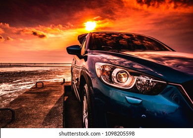 Blue Compact SUV Car With Sport, Modern, And Luxury Design Parked On Concrete Road By The Sea At Sunset. Front View Of Beautiful Hybrid Car. Driving With Confidence. Travel On Vacation At The Beach.