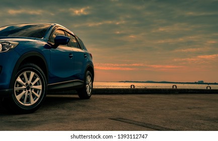 Blue compact SUV car with sport and modern design parked on concrete road by the sea at sunset in the evening. Hybrid and electric car technology concept. Car parking space. Automotive industry. 