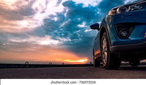 Blue Compact SUV Car With Sport And Modern Design Parked On Concrete Road By The Sea At Sunset. Environmentally Friendly Technology. Car Parking Space. Hybrid And Electric Car Technology Concept.