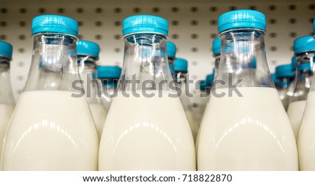 blue covers with small vertical lines on plastic bottles with milk inside against metal background in shop, bottles with milk as dairy product for preparing breakfast wait for byers on market shelf