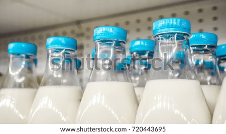 blue covers with small vertical lines on plastic bottles with milk inside against metal background in shop, bottles with milk as dairy product for preparing breakfast wait for byers on market shelf