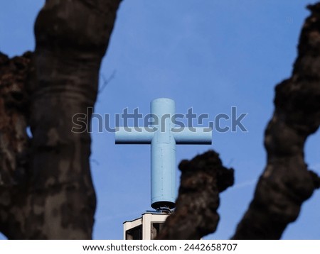 A blue cross stands atop a building near a tree, symbolizing spirituality and faith in an urban setting hiding 5g antenna on rooftop of Eglise Catholique Saint Bernard