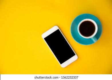 A blue cup with coffee and a mobile phone stands on a yellow background. Morning breakfast, business. - Shutterstock ID 1362232337