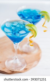 Blue curacao cocktail with lime, ice and mint in martini glasses on wooden background
