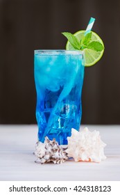 Blue curacao cocktail with lime, ice and mint in glasses on wooden background