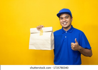 Blue Delivery Handsome Asian Man Holding Paper Bag On Isolated Yellow Background.