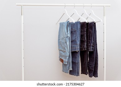 Blue denim jeans hanging on white clothes hangers on portable clothing rack. Casual denim jeans in dressing room on white background, copy space