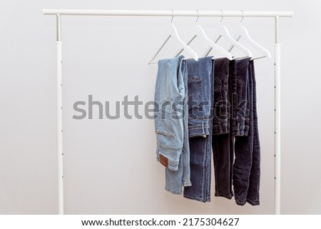 Blue denim jeans hanging on white clothes hangers on portable clothing rack. Casual denim jeans in dressing room on white background, copy space