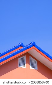 Blue Different Level Ridge Capping Tiled Roofs With 2 White Attic Windows Of Orange House Against Blue Clear Sky In Vertical Frame