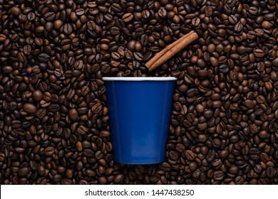 A Blue Disposable Cup Of Coffee To Go With A Cinnamon Stick Against The Background Of Roasted Beans