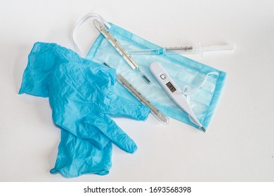 Blue Disposable Gloves, Mask, Electronic And Mercury Thermometers, Empty Syringe Are On The White Background