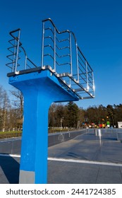 A blue diving board over an empty swimming pool. Stainless steel rails around the platform. The outdoor swimming pool is ready for the seasonal break.