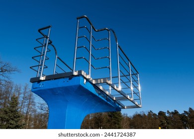 A blue diving board over an empty swimming pool. Stainless steel rails around the platform. The outdoor swimming pool is ready for the seasonal break.