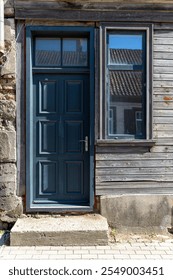 A blue door with a rectangular window beside it welcomes visitors to an old structure.