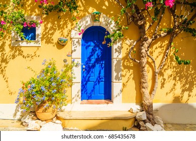 Blue door of a yellow Greek house decorated with flowers, Assos town, Kefalonia island, Greece