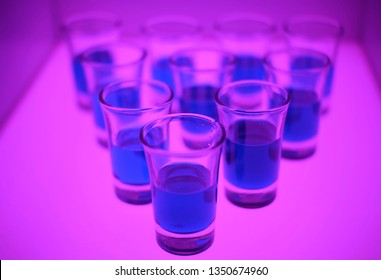 A blue drink in a shot glasses is bowling line up in a light box. - Powered by Shutterstock