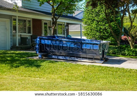 A blue dumpster in the driveway of a house in a residential neighborhood